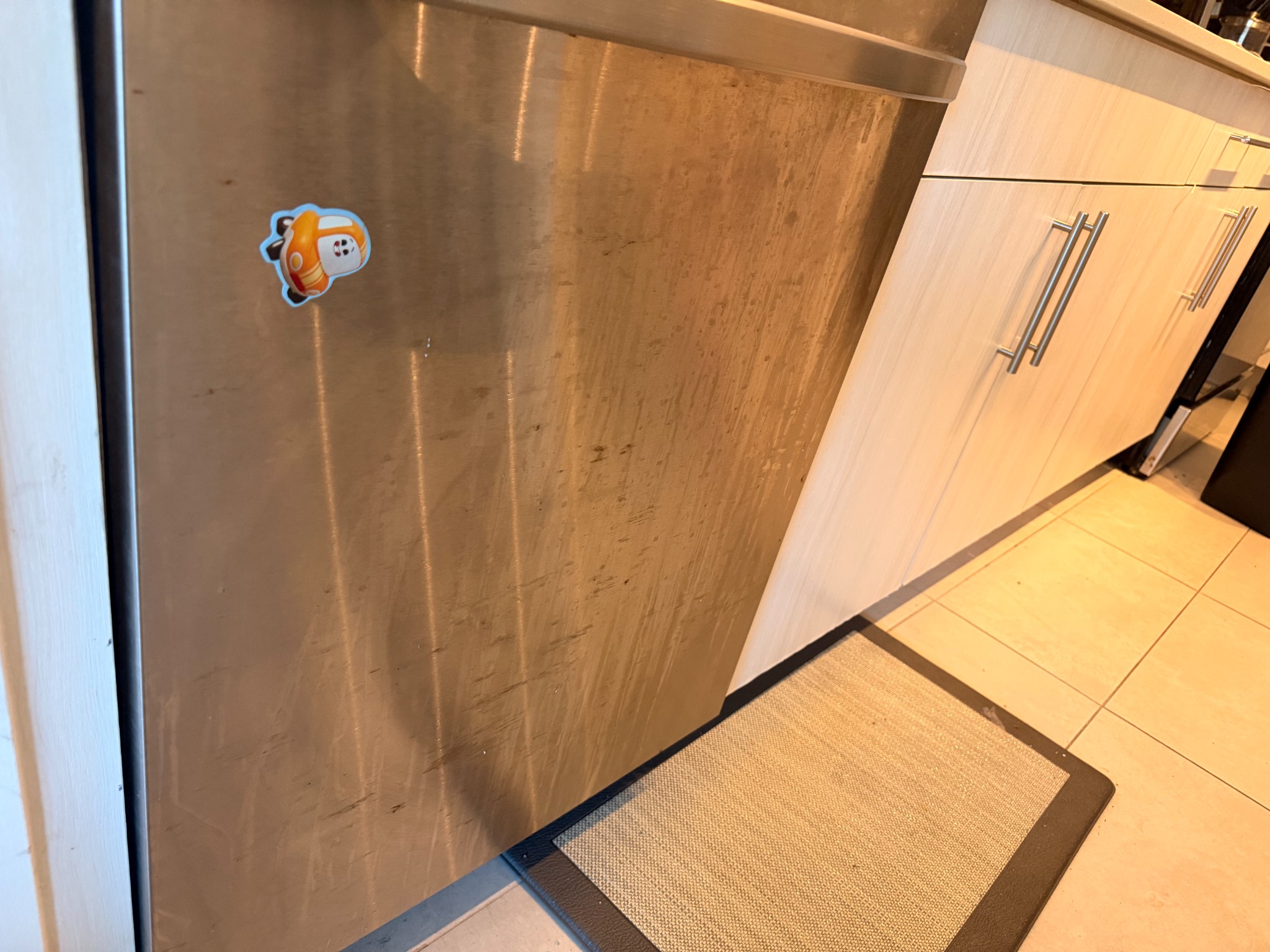 Stainless-steel dishwasher door with smudges and streaks before cleaning.
