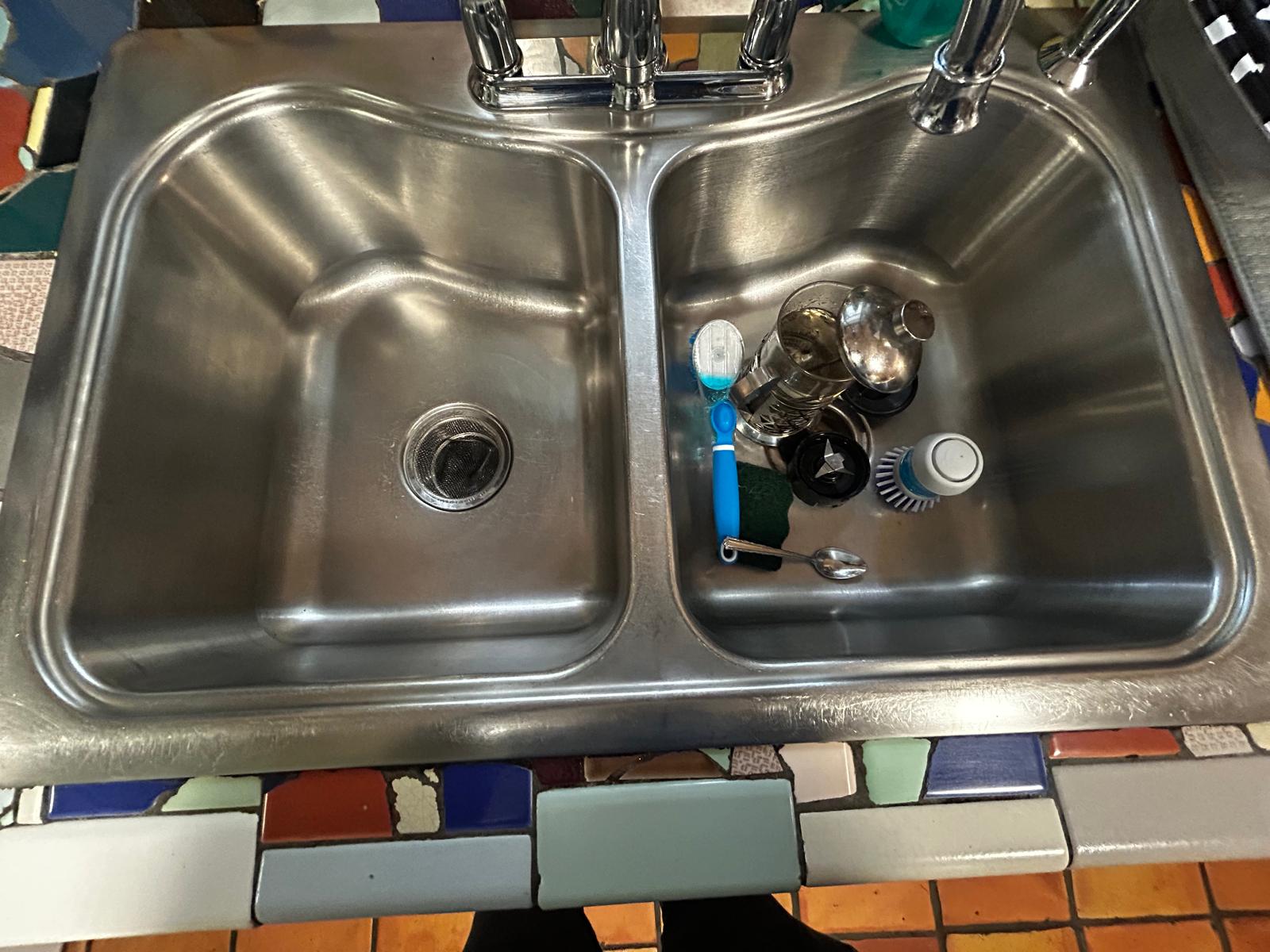 Stainless-steel kitchen sink after cleaning, with debris and visible buildup removed.