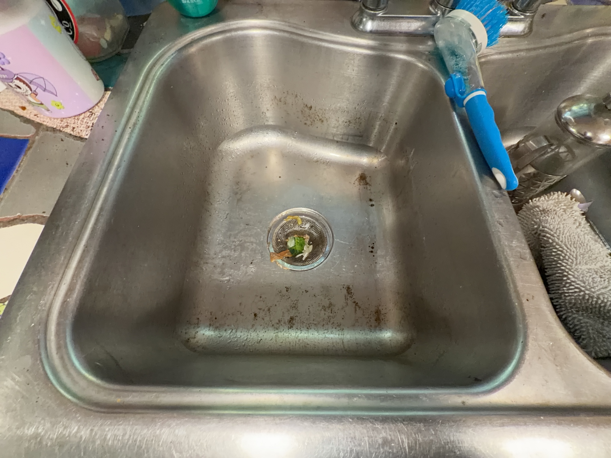 Stainless-steel kitchen sink with visible residue and food debris before cleaning.