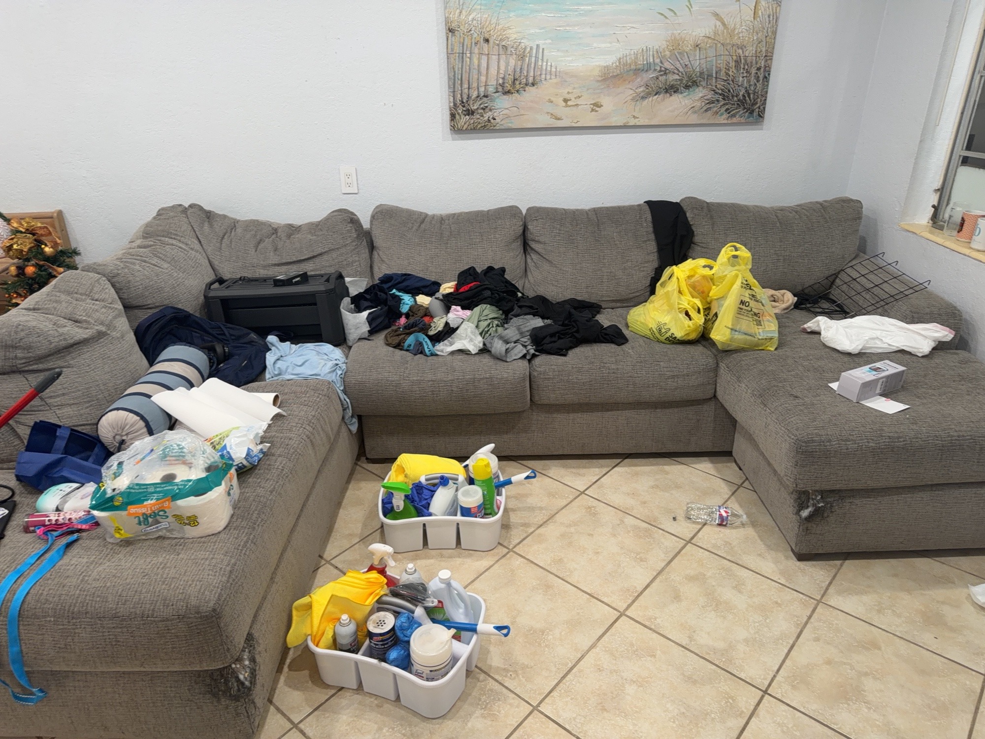 Living room with loose clothing and household items on the sectional and floor before tidying.